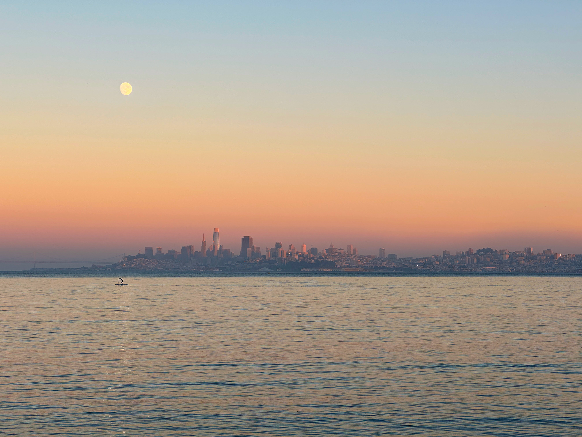Moon rising over the San Francisco skyline, with the sky a rainbow color at sunset.